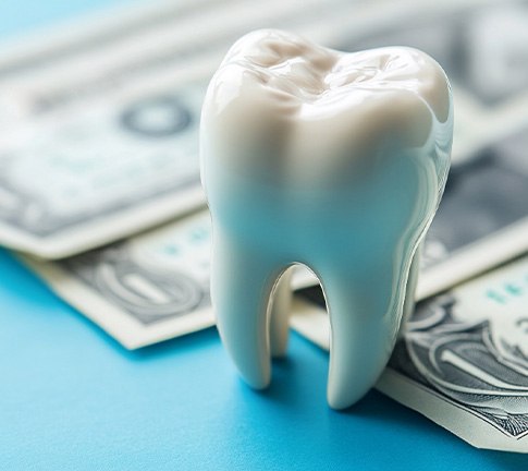 Large model tooth next to dollar bills on blue surface