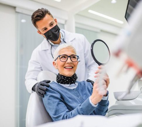 Patient admiring their new teeth in mirror with dentist standing behind them