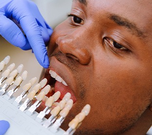 Dentist’s gloved hands holding shade guide to man’s teeth