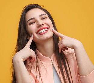 Woman with long brown hair pointing to her smile with both pointers