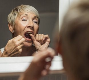 Woman flossing in bathroom mirror