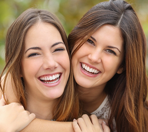 Two brown-haired women outside smiling and hugging