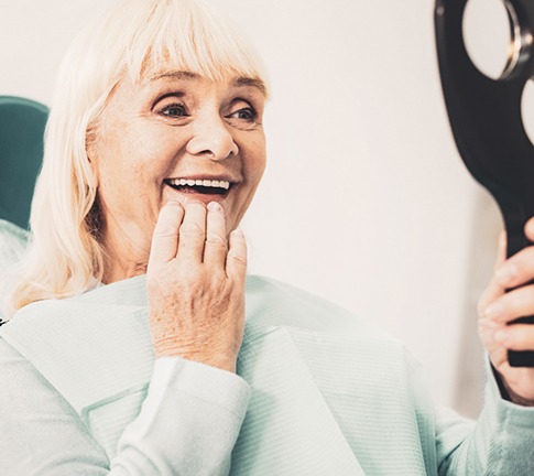 A mature woman admiring her dentures in a hand mirror