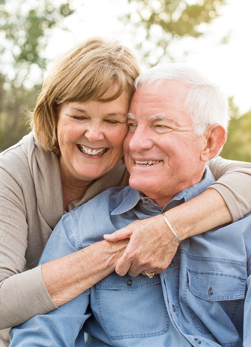 A smiling senior couple hugging outdoors