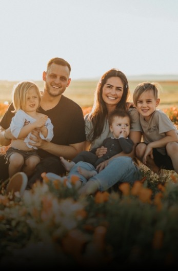 Mother father and three young children sitting in field of flowers