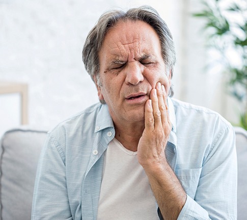 Man sitting on couch while rubbing jaw in pain