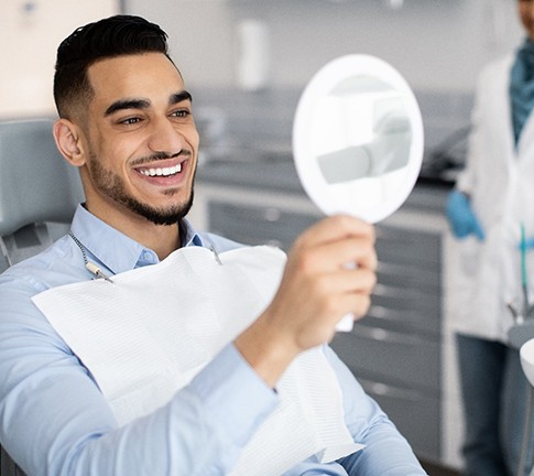 Man smiling at reflection in handheld mirror