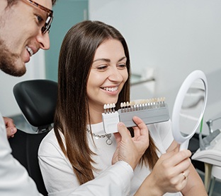 Woman smiling at reflection while dentist uses shade scale