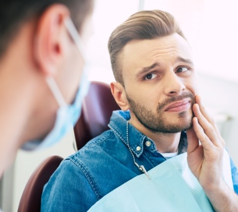 Young man in need of wisdom tooth extraction holding cheek in pain