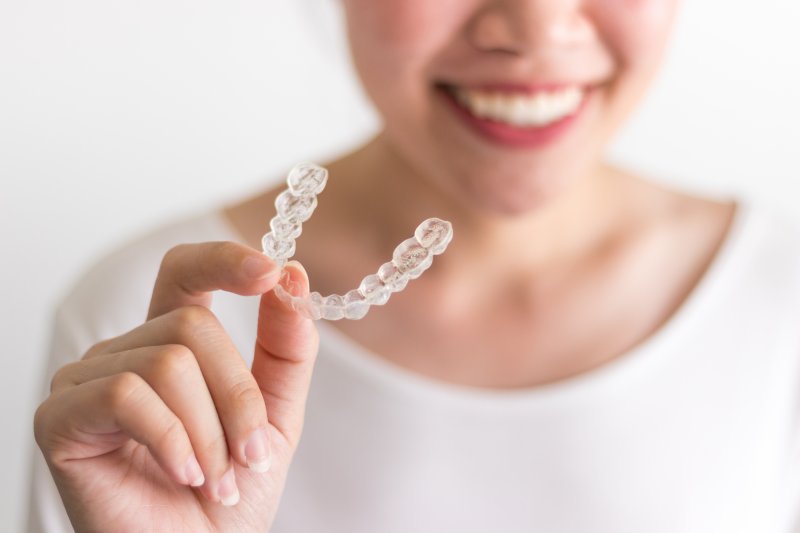 Smiling woman holding her Invisalign aligner