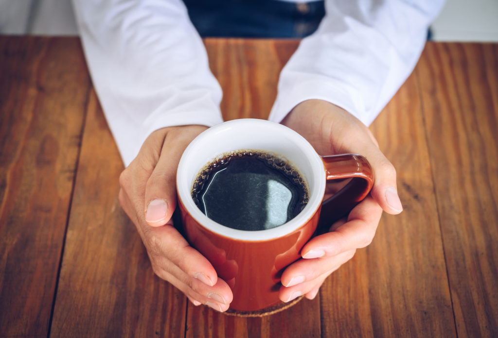 person with hands wrapped around coffee mug