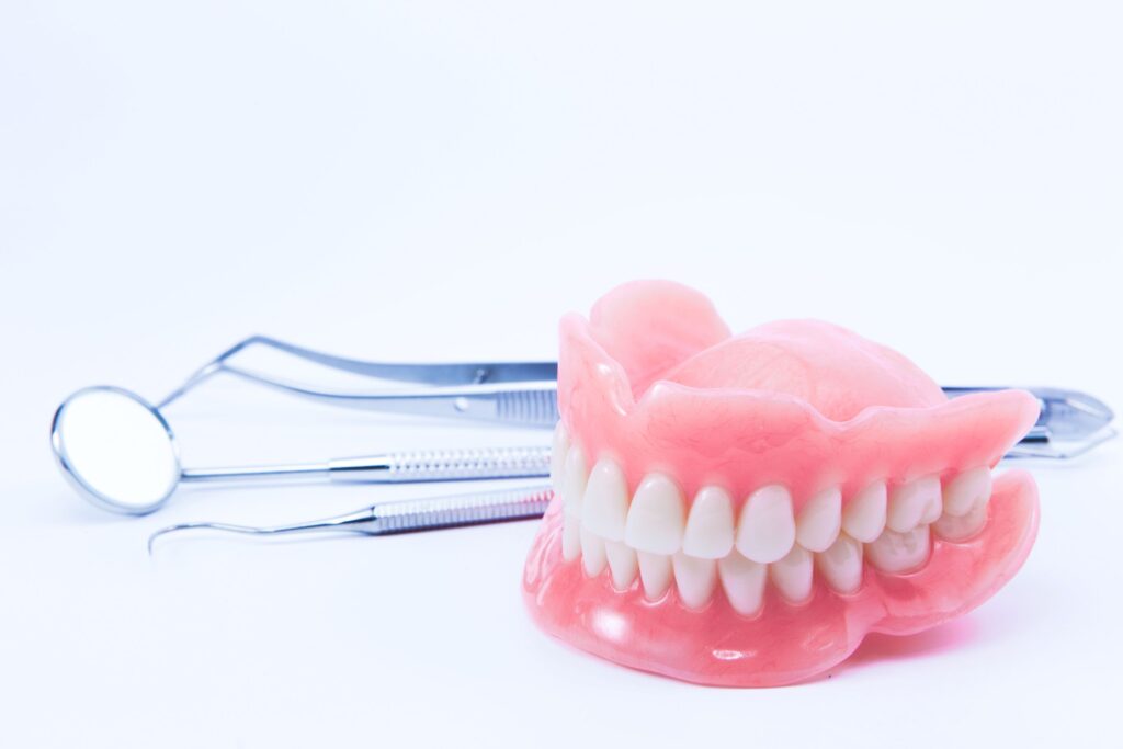 Complete set of dentures on white surface next to dental instruments