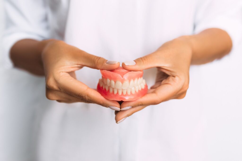 Dentist in white holding dentures with both hands at her midsection